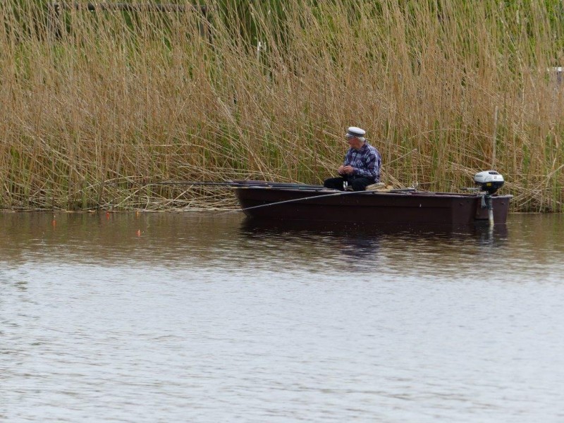 Ein alter Fischer der in seinem Boot bei schlechtem Wetter, in der Peene in Mecklenburg Vorpommern angelt.