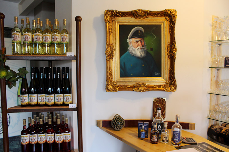 Blick über den Tresen und Regale mit Torfkopp Wein, Bier und Westlind Whisky. Dahinter hängt ein Bild mit einem alten Torfkahn Kapitän.