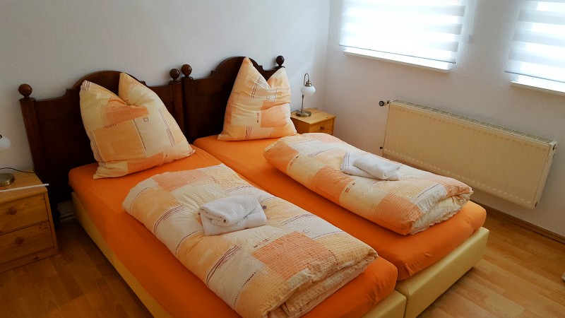 Hotelzimmer mit geschnitzem Holz-Doppelbett und frischem orangenem Bettbezug und Bettwäsche mit Fenster zum Wasser.
